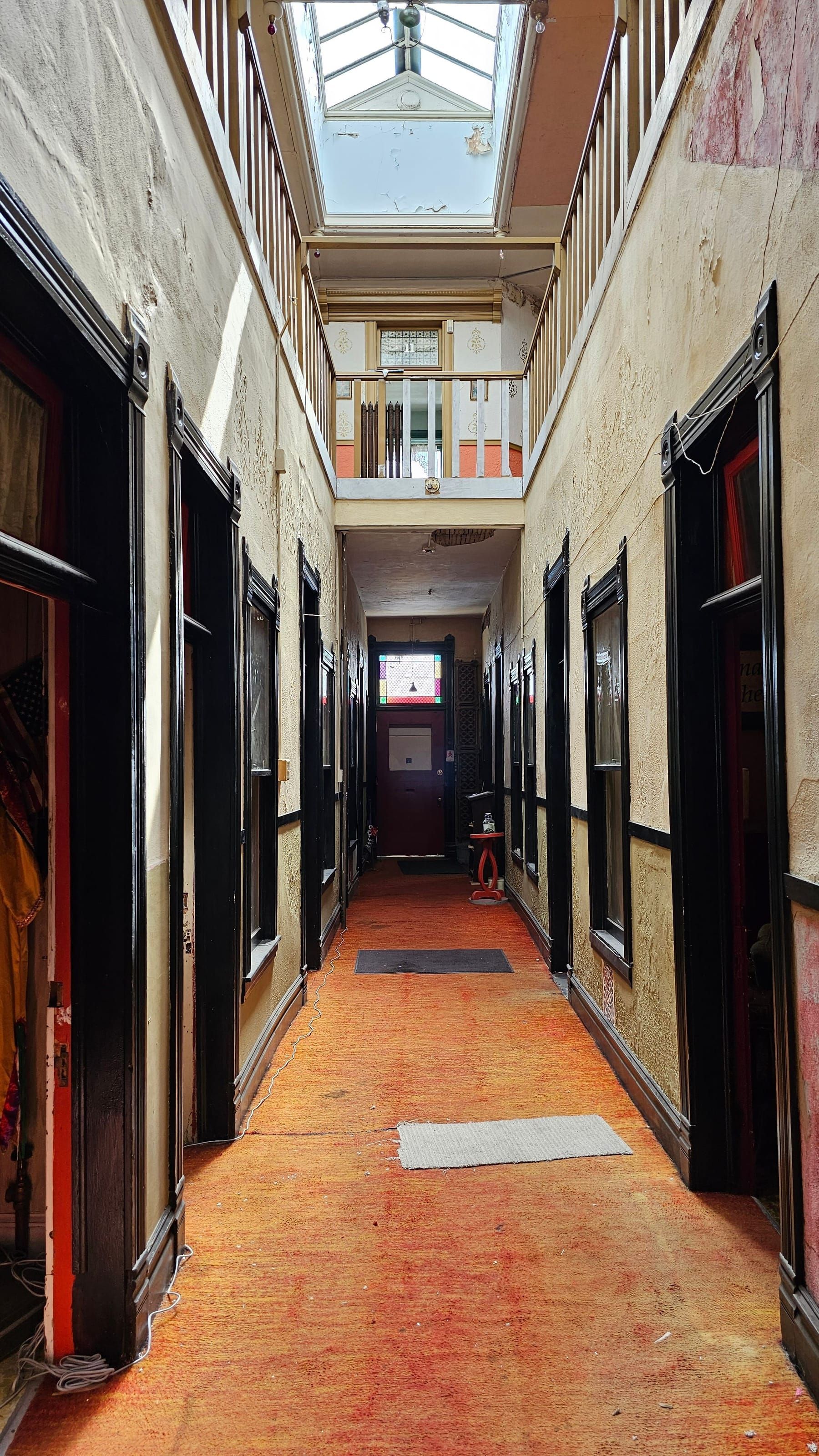 The skylit interior corridor of the Dumas, doors to the cribs lining a worn orange runner, stained-glass door at the far end