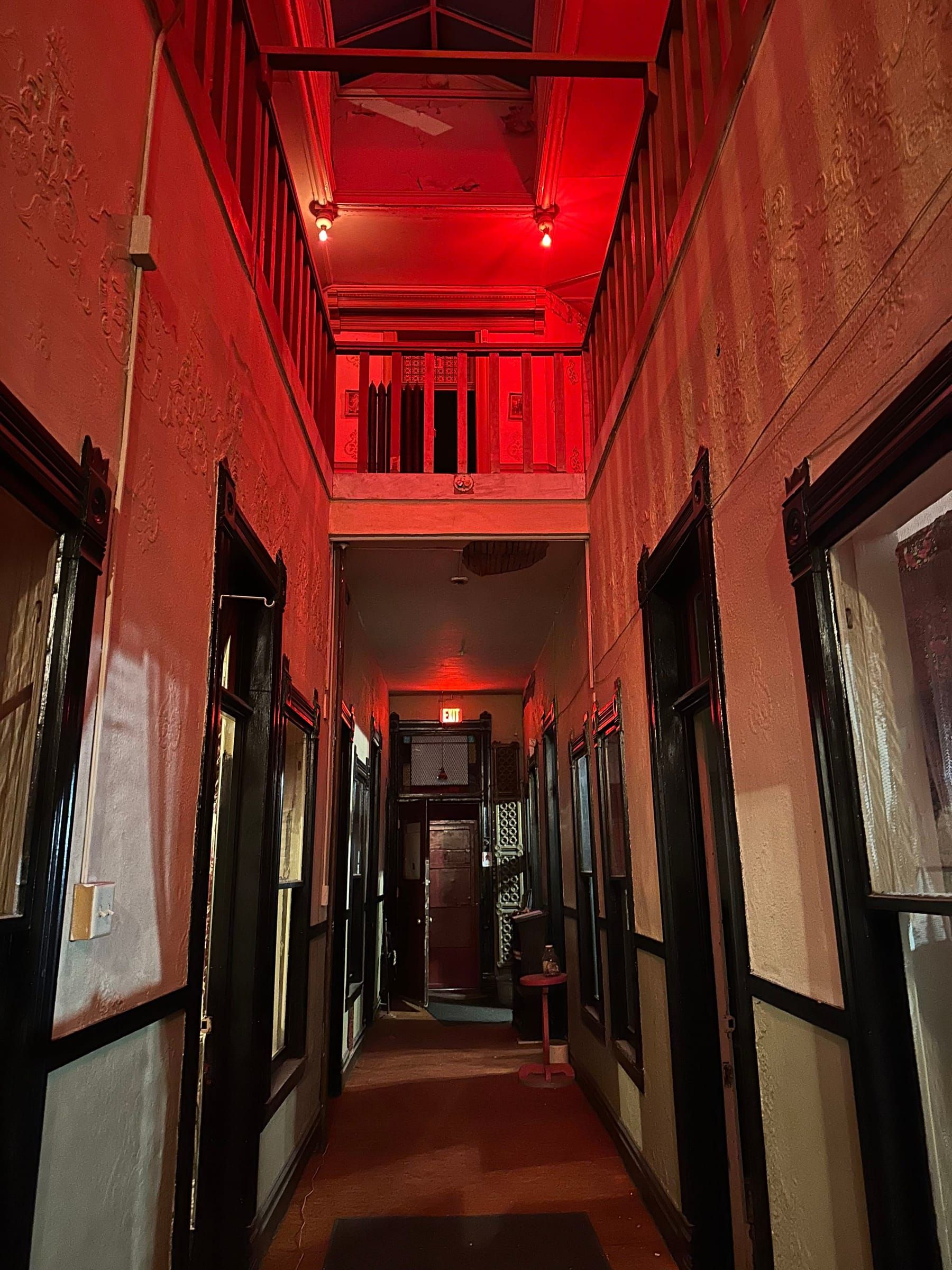 The Dumas corridor under red light after dark, crib doors lining a dim hallway
